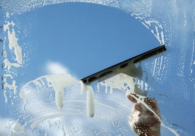 Professional window cleaning with squeegee in bright sunlight