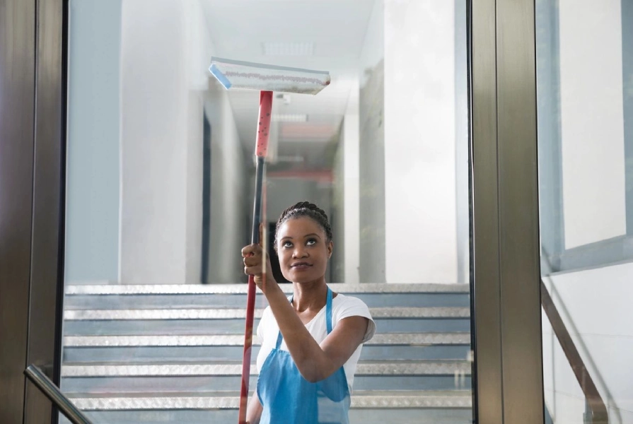 A woman holding a mop in front of stairs.