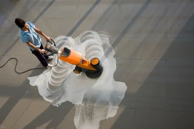 A person is using an electric floor scrubber.